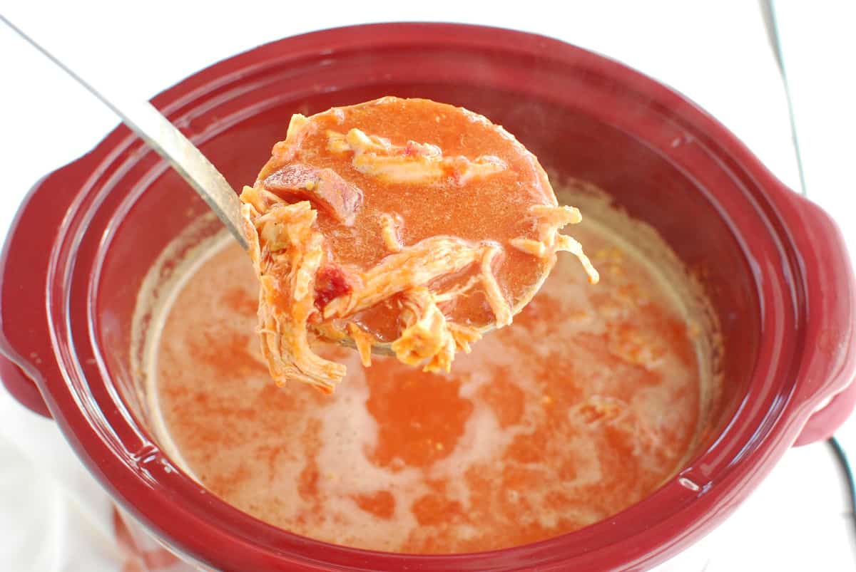 A ladle full of butternut squash beet soup over a crockpot.