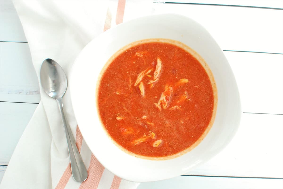 A bowl of butternut squash beet soup with chicken, next to a napkin and a spoon.