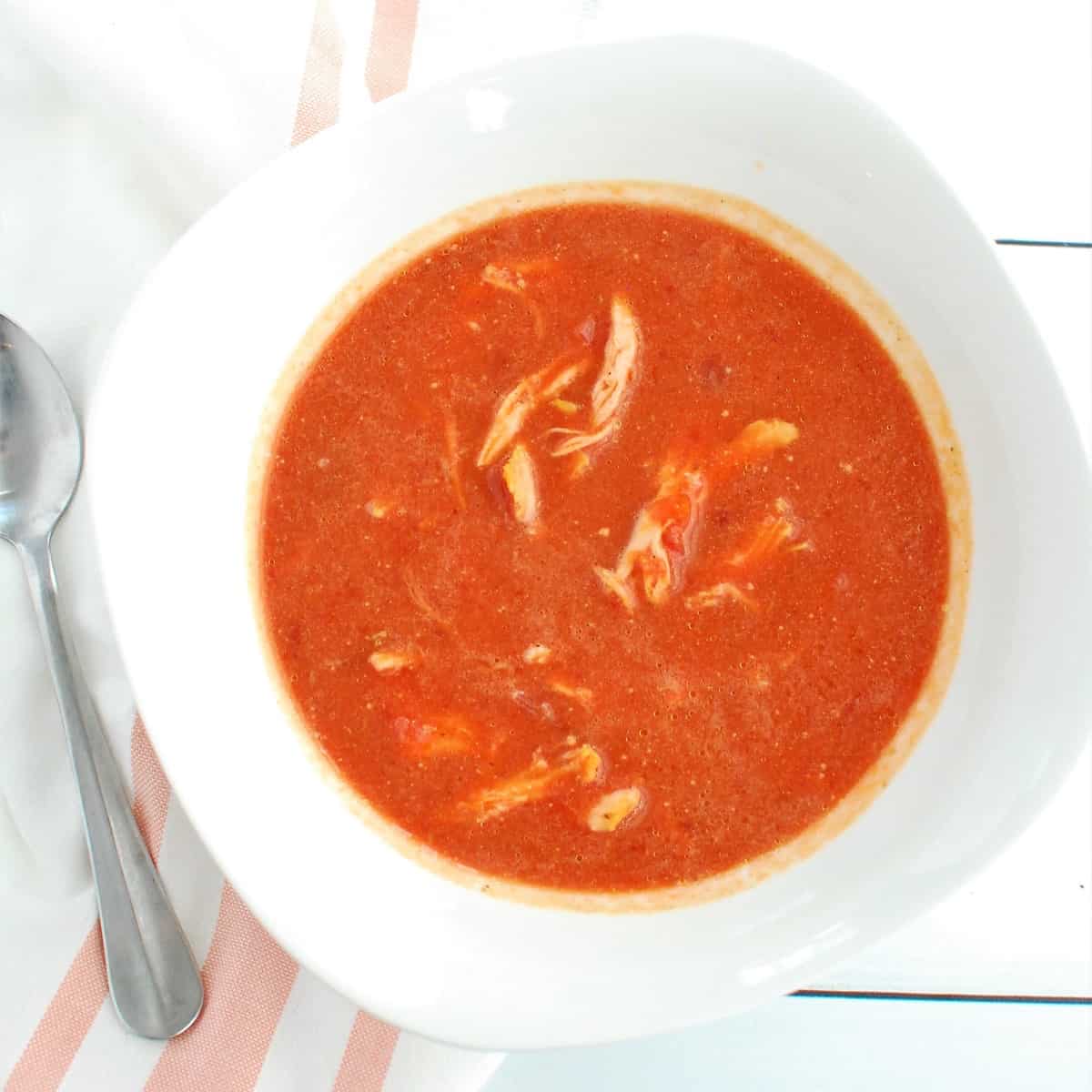 A white bowl filled with butternut squash and beet soup, next to a napkin and spoon.