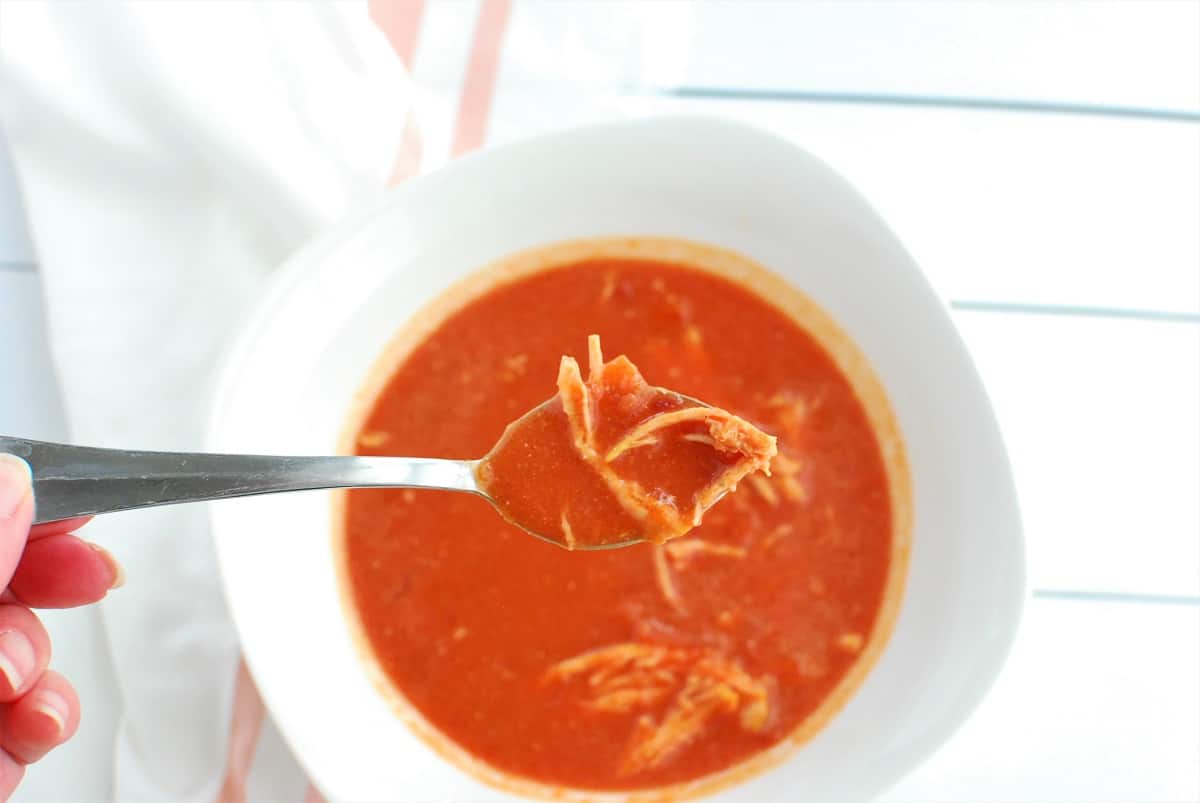 A woman's hand holding a spoonful of butternut squash beet soup with chicken.