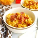 A bowl of pumpkin butternut squash pasta garnished with bacon with additional ingredients in the background.