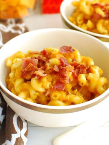 A bowl of pumpkin butternut squash pasta garnished with bacon with additional ingredients in the background.