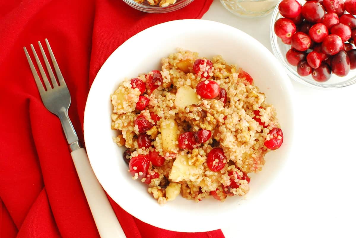 Overhead shot of a bowl of cranberry apple breakfast quinoa, next to a fork and fresh cranberries.