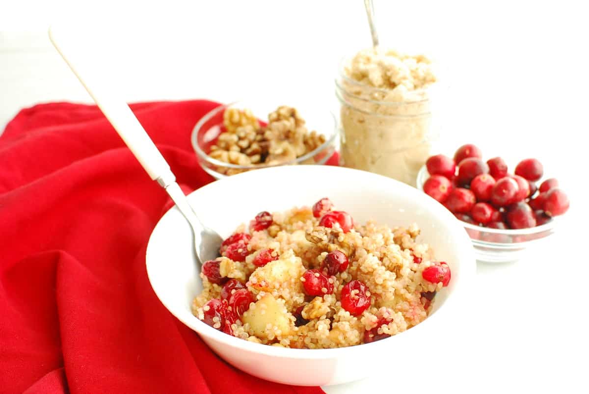 A cranberry apple quinoa breakfast bowl, next to brown sugar, cranberries, and walnuts.