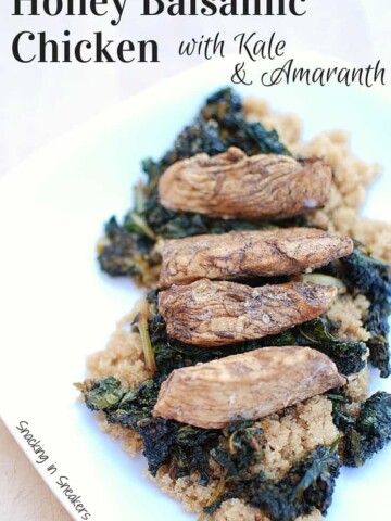 A plate of honey balsamic chicken over kale and amaranth, place on a wooden board.