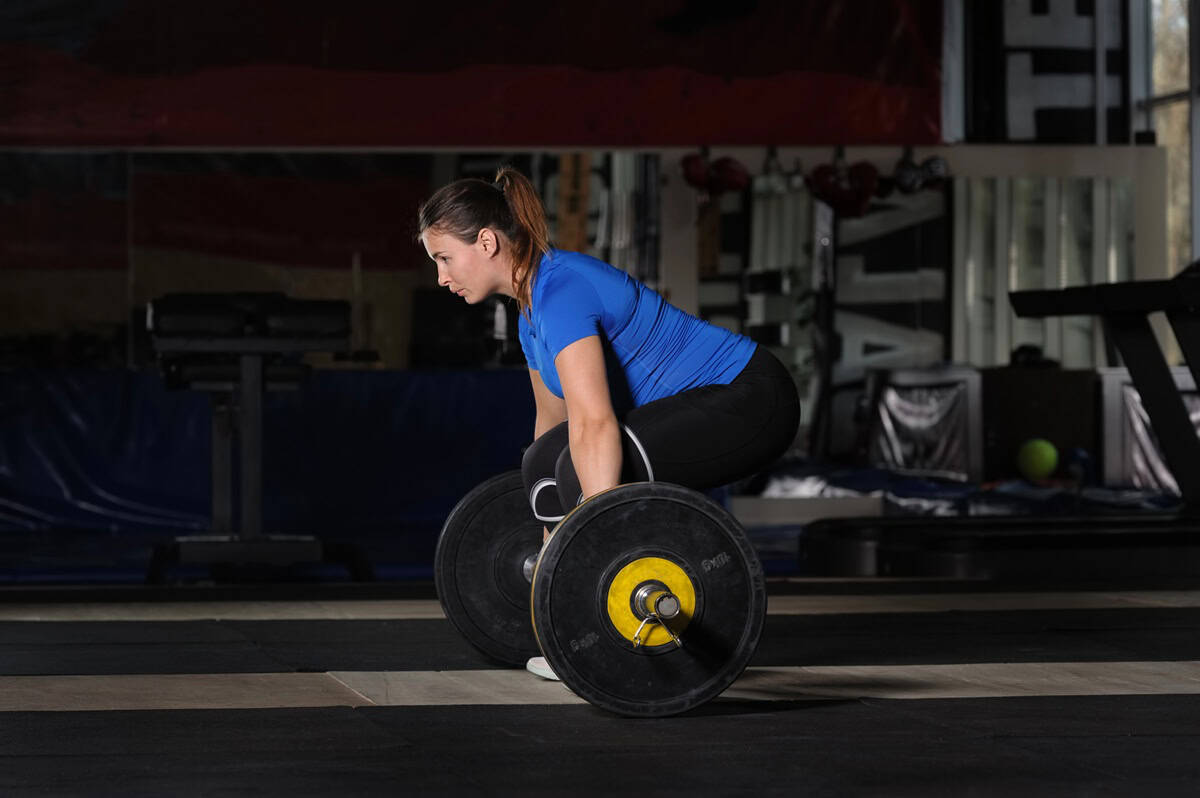 A female runner doing a deadlift strength training exercise in a gym.
