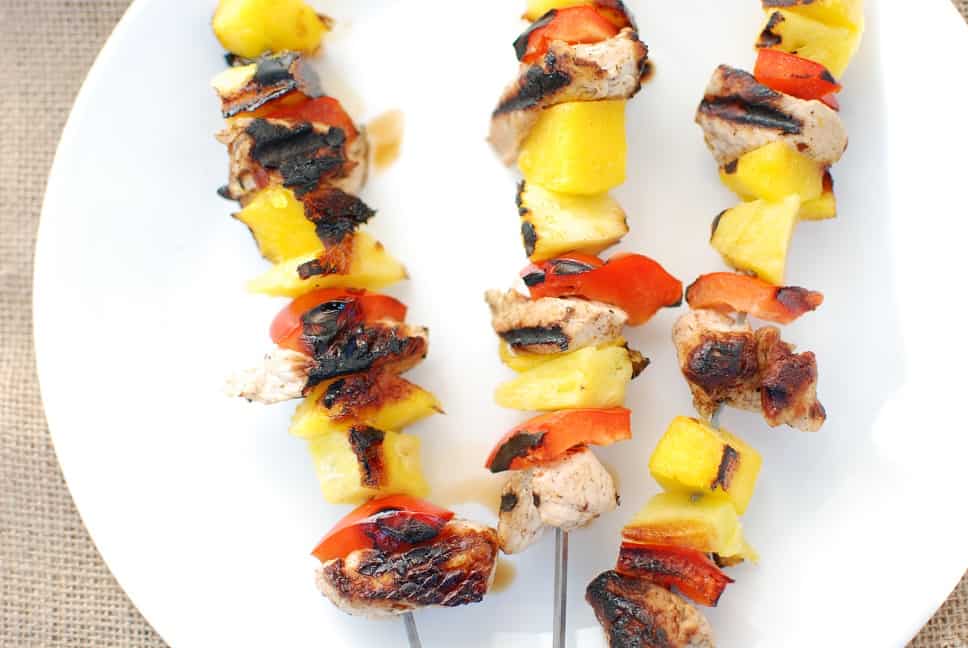 Three grilled turkey skewers with peppers and pineapple on a white plate