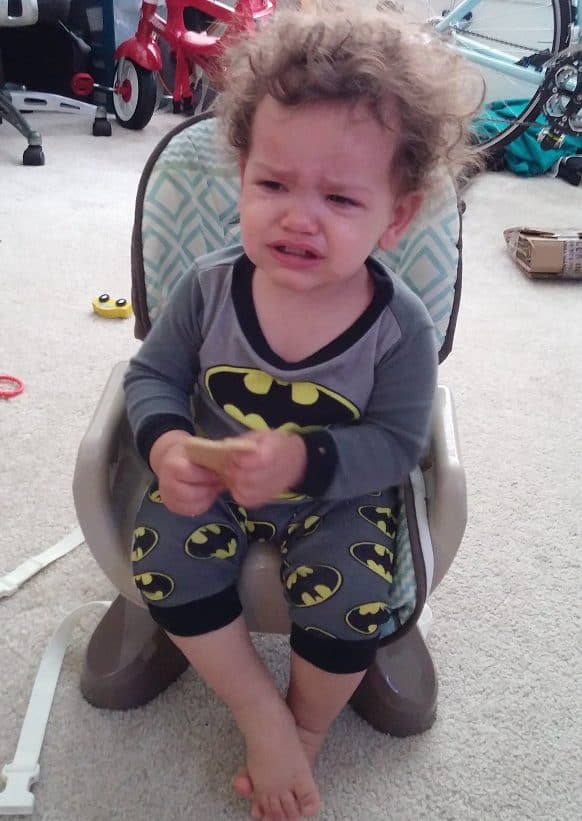 A toddler crying in a high chair seat.