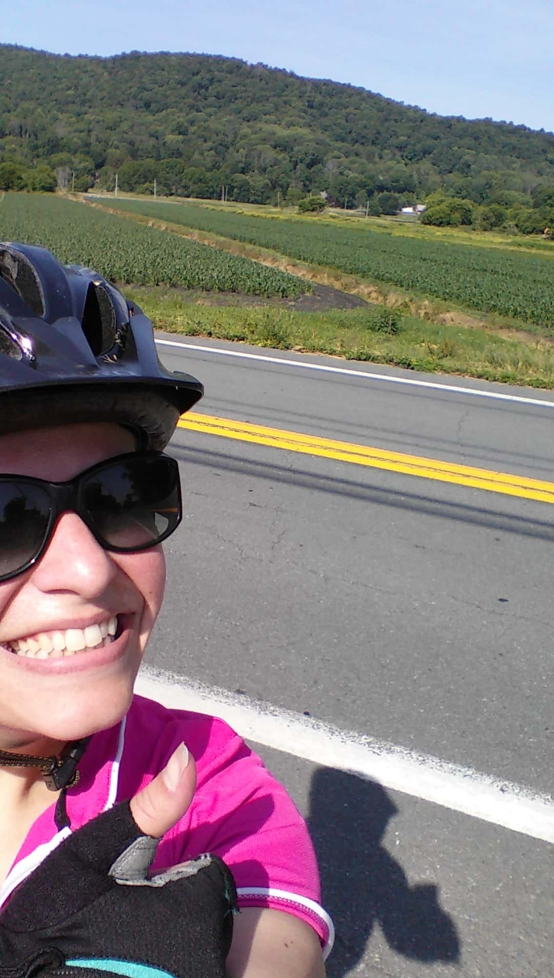 A woman giving a thumbs up on her bicycle outside on a sunny day.