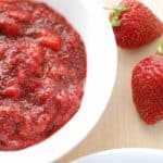 A bowl full of strawberry chia jam next to some fresh strawberries.