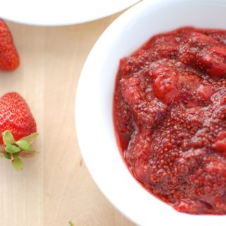 A bowl of strawberry chia jam, next to some fresh strawberries.