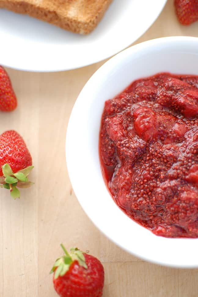 A bowl full of strawberry chia jam next to some fresh strawberries.