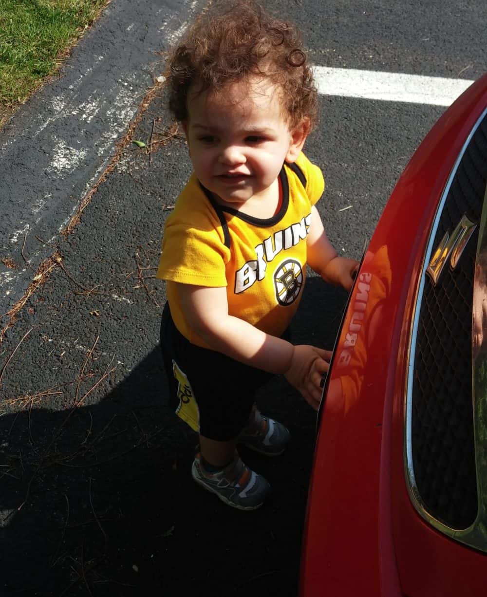 A toddler standing next to a car outside.