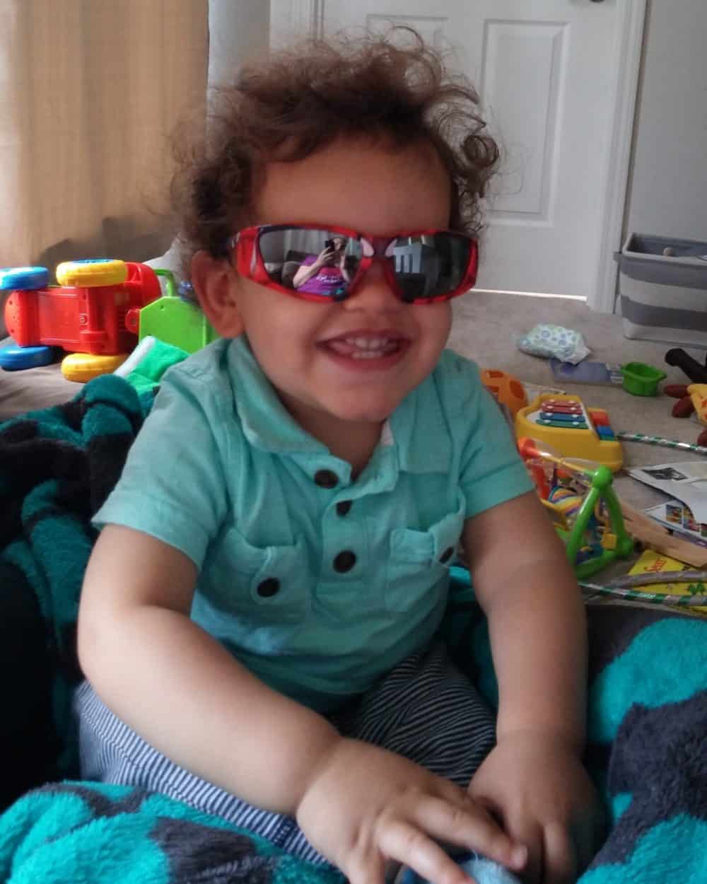 A toddler wearing sunglasses in his room.