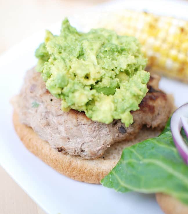 An open faced southwestern turkey burger topped with guacamole.