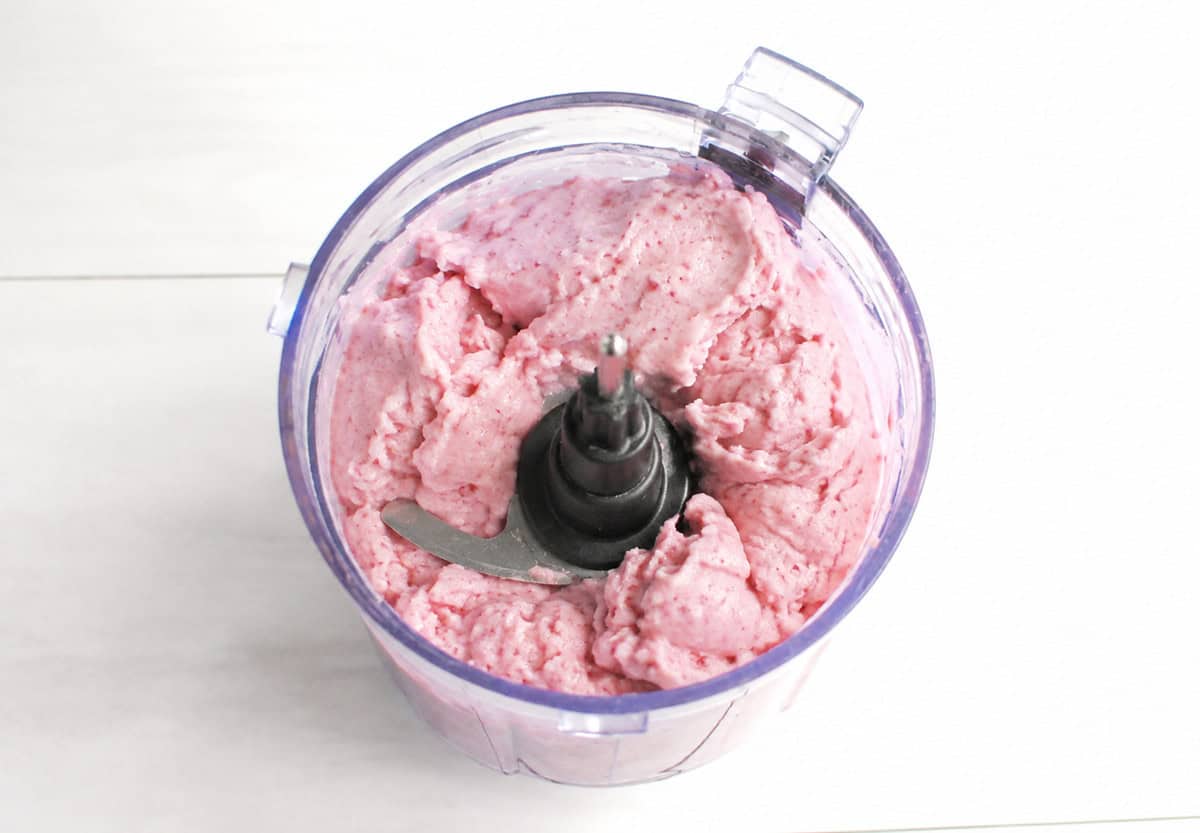 Bananas, strawberries, and dairy-free milk blended together in a mini food processor bowl.