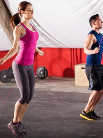 A man and a woman jump roping in a gym.