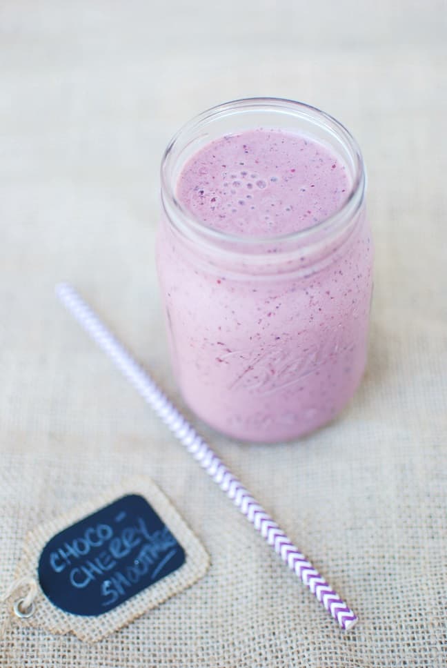 A pink smoothie in a mason jar, next to a purple straw