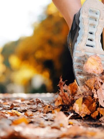 Sneakers on the ground running in fall leaves.