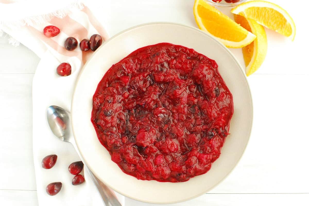 A bowl of lower sugar cranberry sauce with a napkin, spoon, and fresh cranberries next to it.