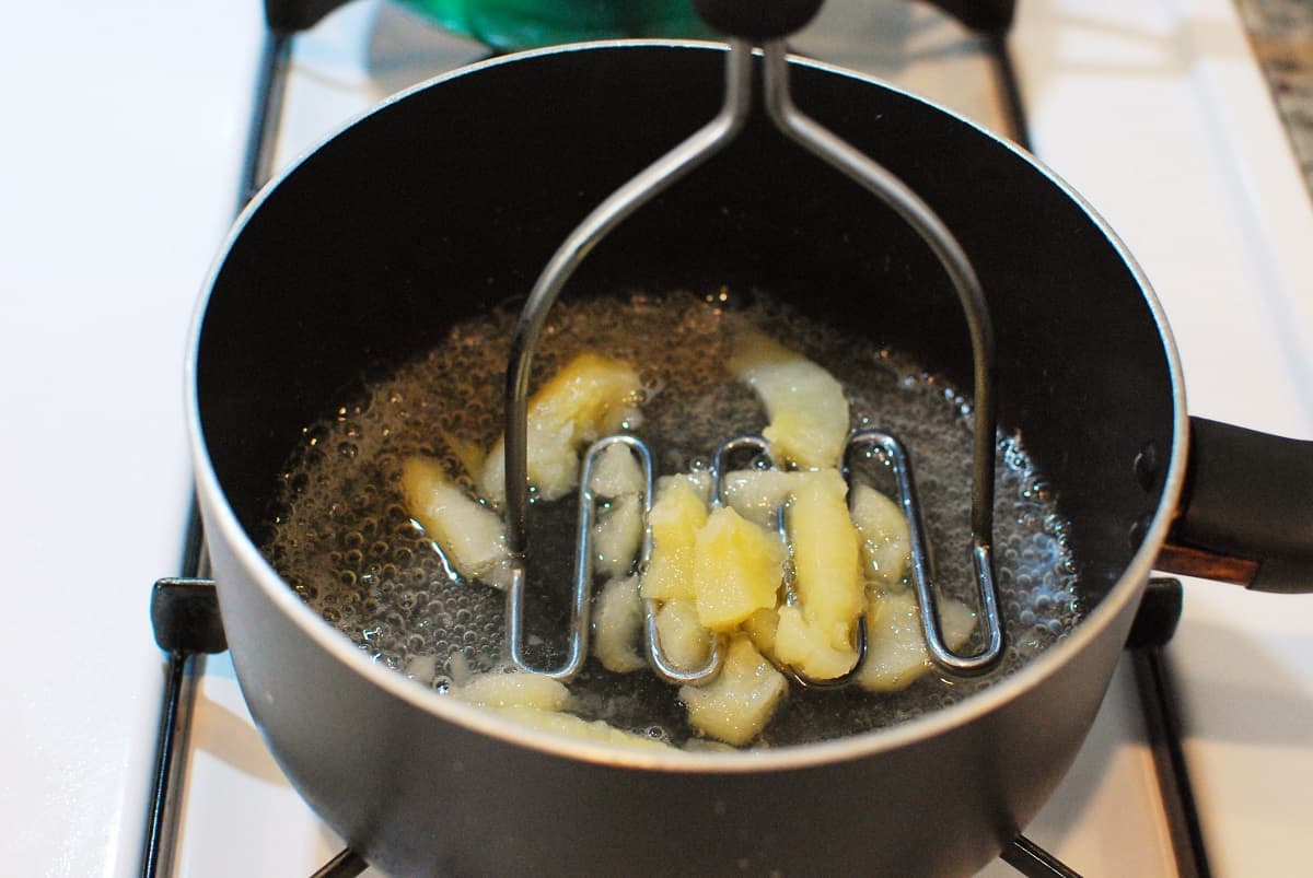 Mashing the pears in the pot with a potato masher.