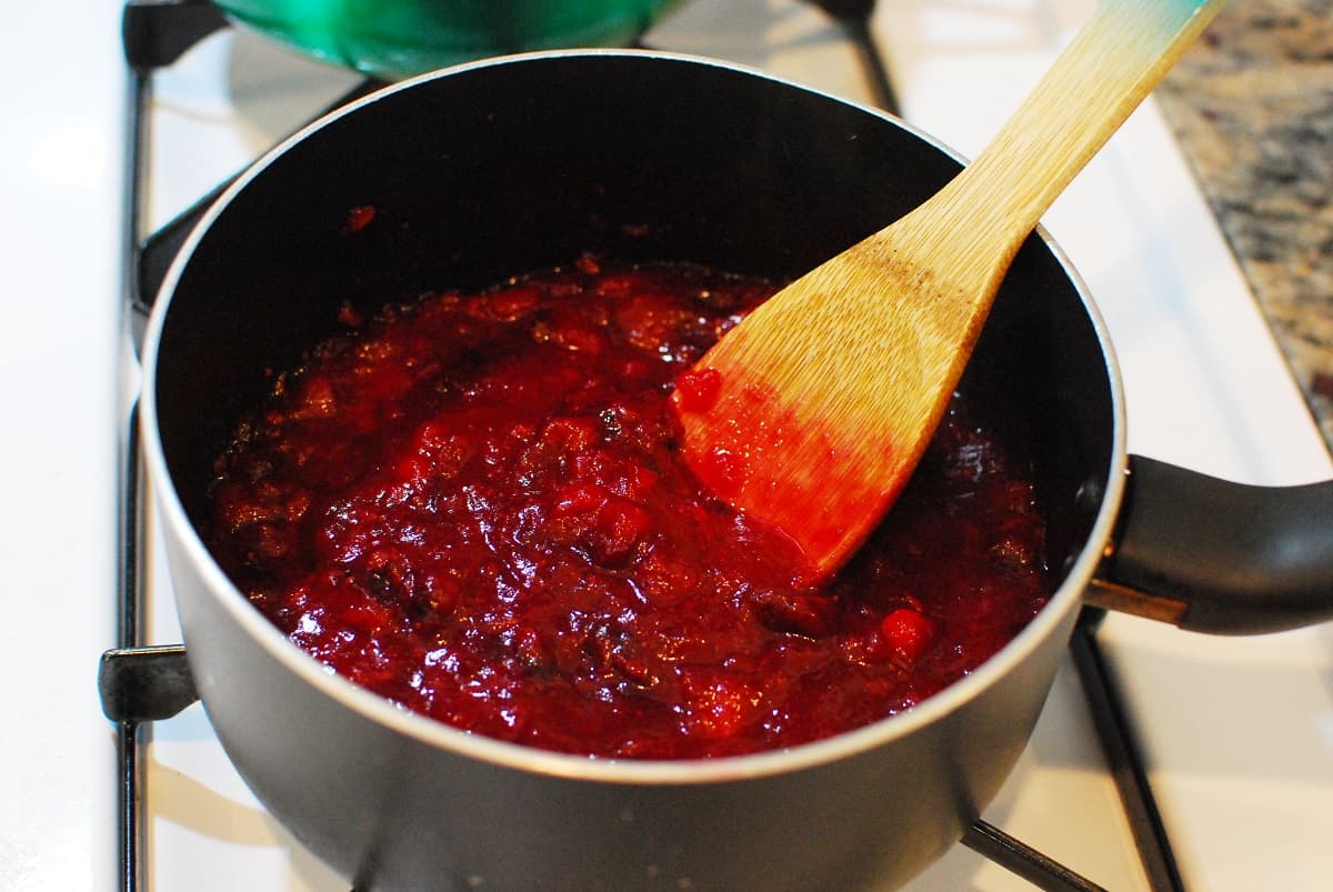 A pot of cranberry sauce with a wooden spoon in it.