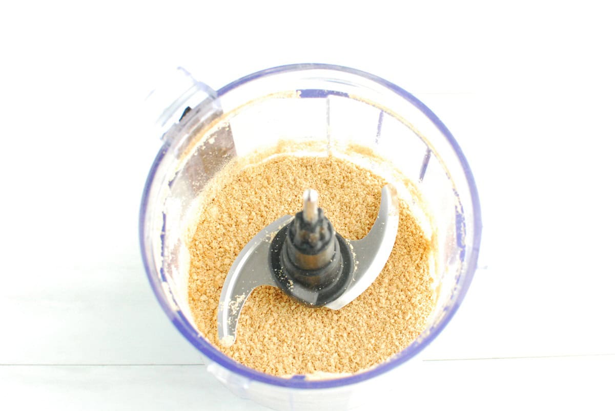 A mini food processor bowl with ground graham crackers in it.