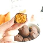 A hand holding a no bake pumpkin truffle with a bite taken out of it.