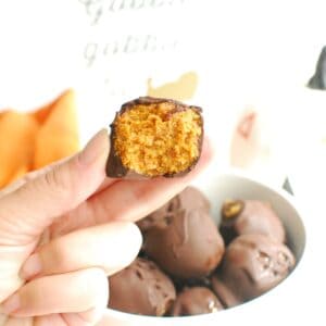 A hand holding a no bake pumpkin truffle with a bite taken out of it.