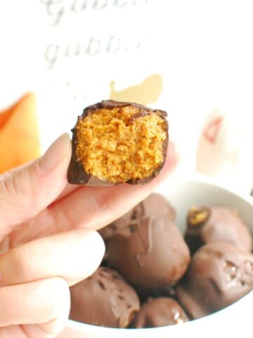 A hand holding a no bake pumpkin truffle with a bite taken out of it.