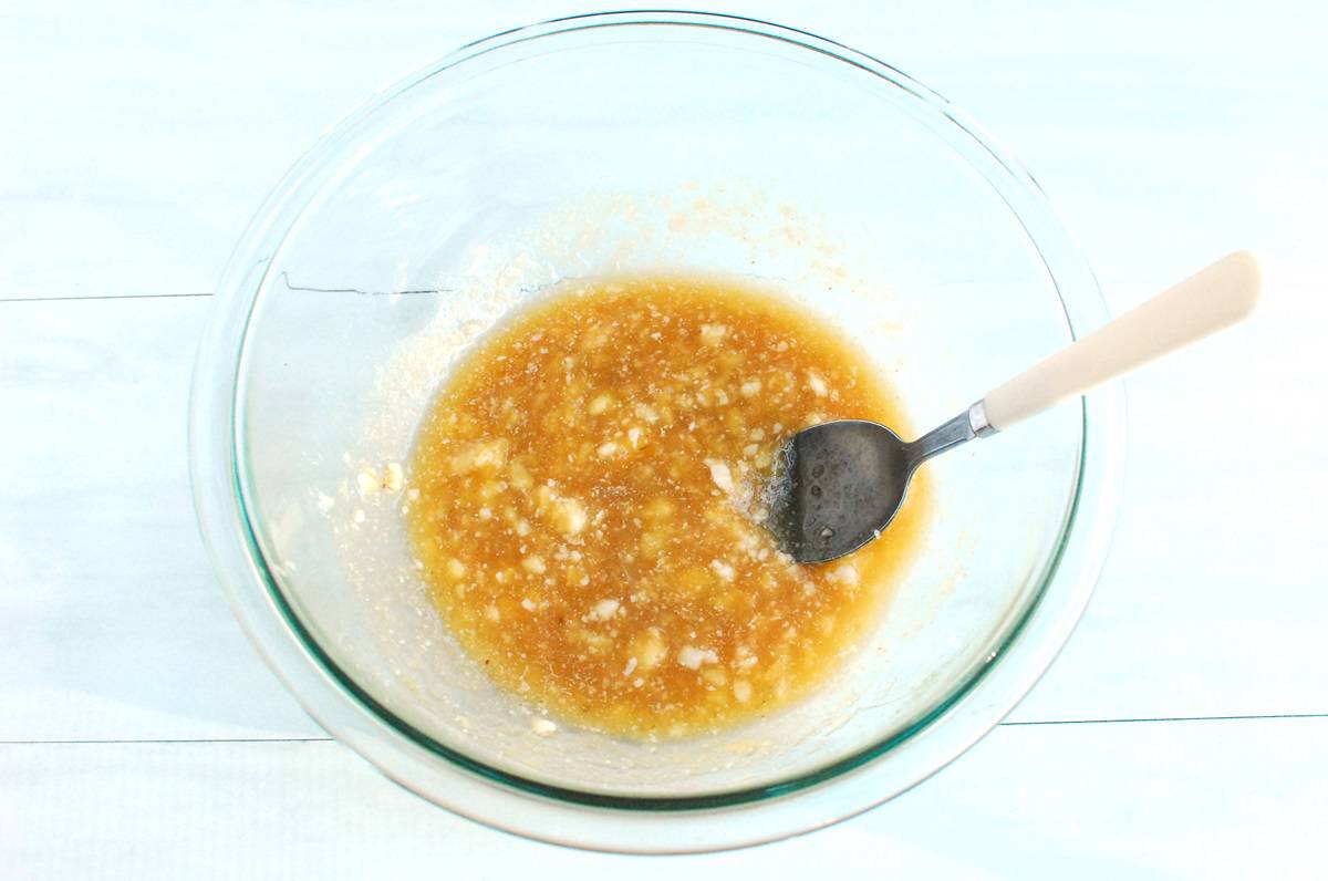 Banana, maple syrup, applesauce, coconut oil, and vanilla mixed together in a glass bowl.