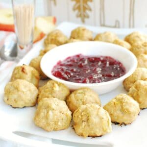Chicken apple meatballs on a white plate next to a small bowl of cranberry sauce and a container of toothpicks.