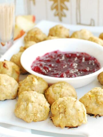 Chicken apple meatballs on a white plate next to a small bowl of cranberry sauce and a container of toothpicks.