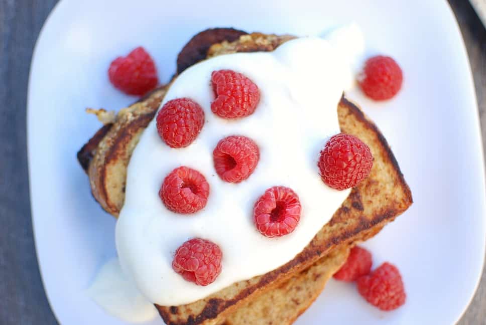 A white plate with full slices of eggnog french toast topped with raspberries.