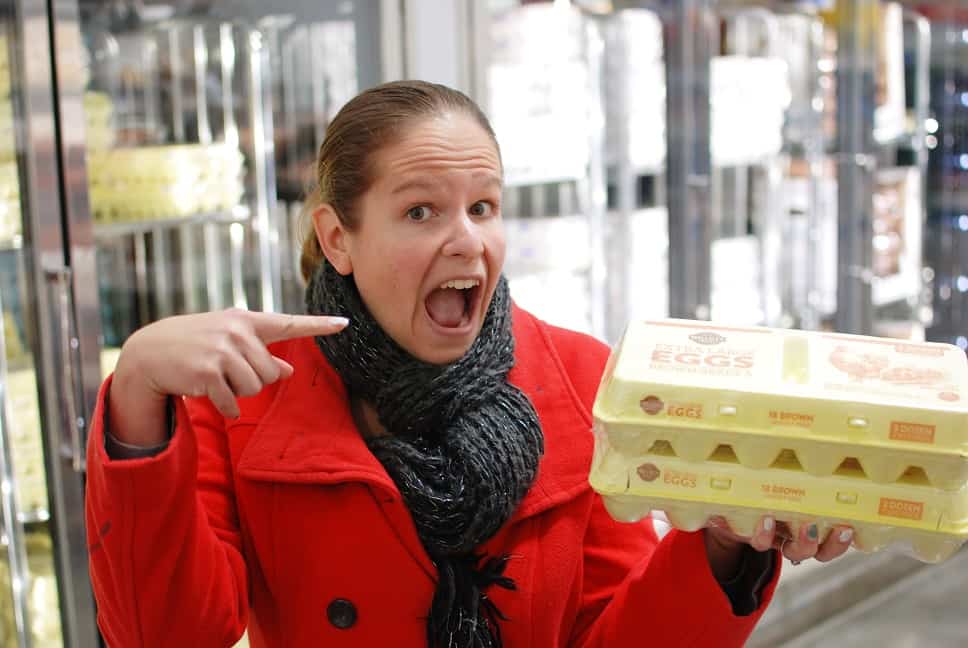 A woman at a grocery store holding two containers of eggs.