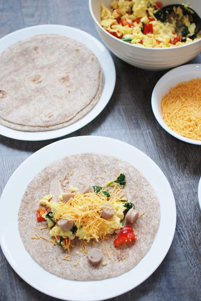 A plate with a tortilla with an egg, sausage, veggie, and cheese mixture added on top of it.