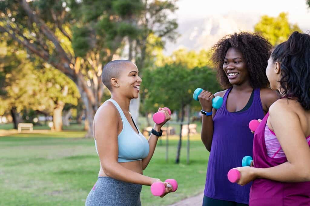 Three women doing exercise with weights together at a park.