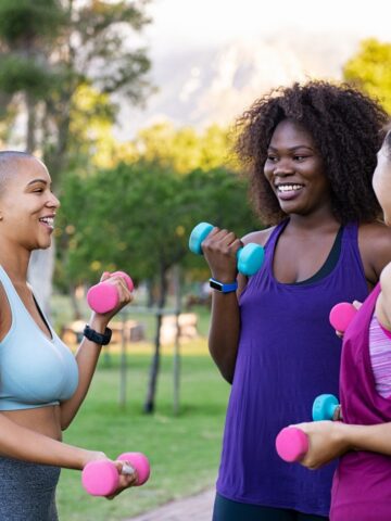 Three women doing exercise with weights together at a park.
