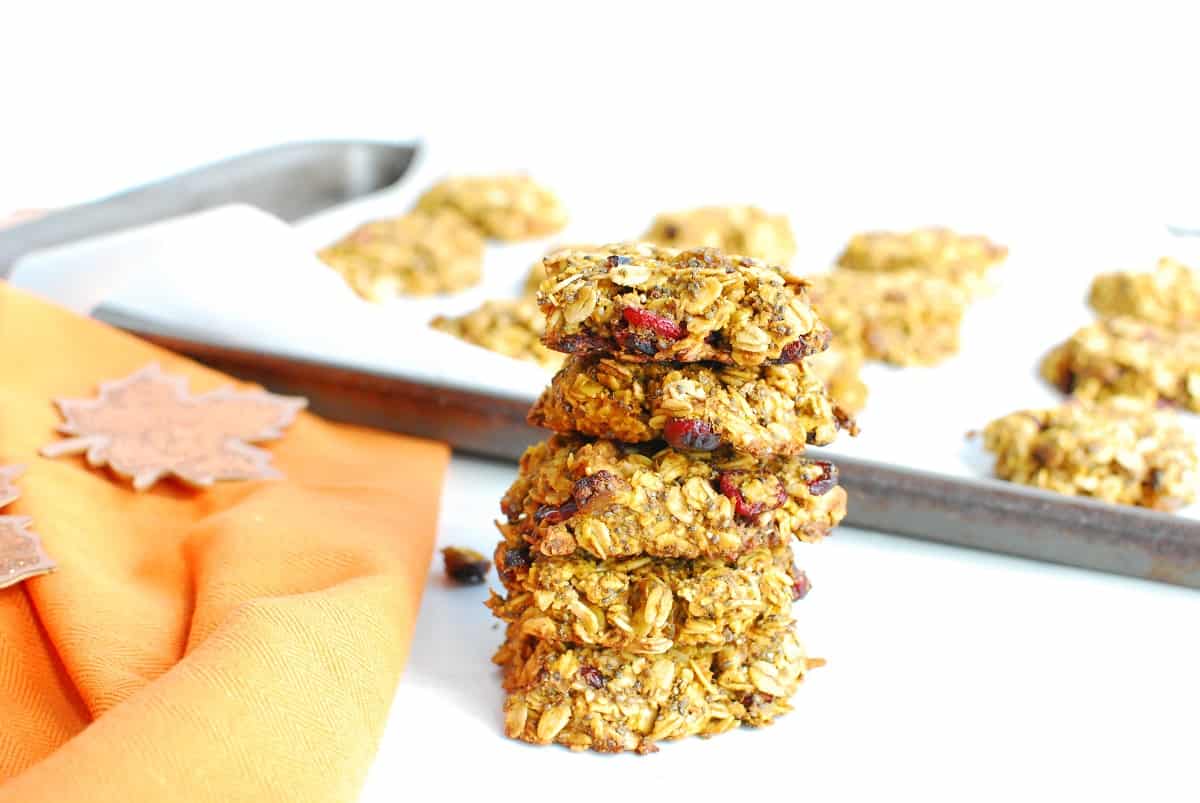 A stack of several pumpkin oatmeal breakfast cookies next to an orange napkin and a baking sheet.