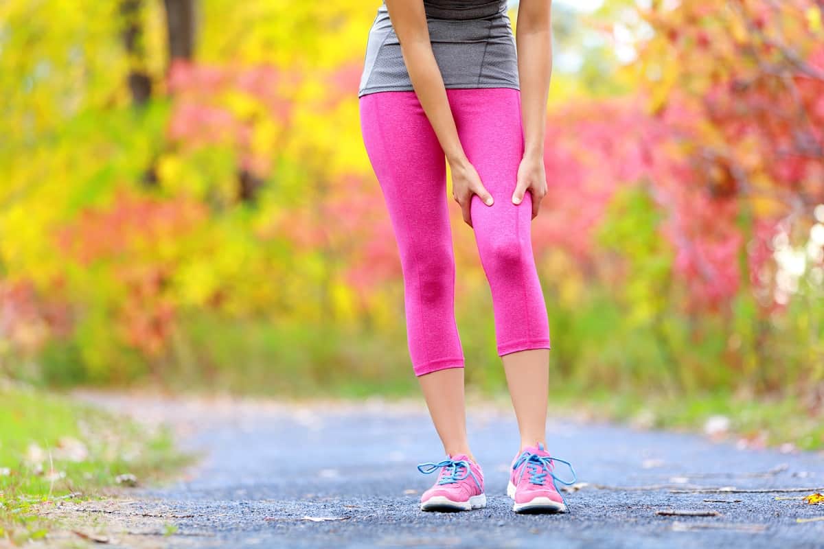 A woman grabbing her hamstring with a muscle cramp during a run.