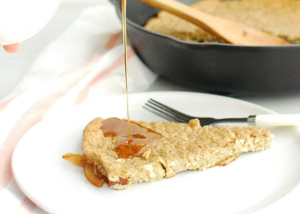 A slice of skillet apple pancake being drizzled with maple syrup.