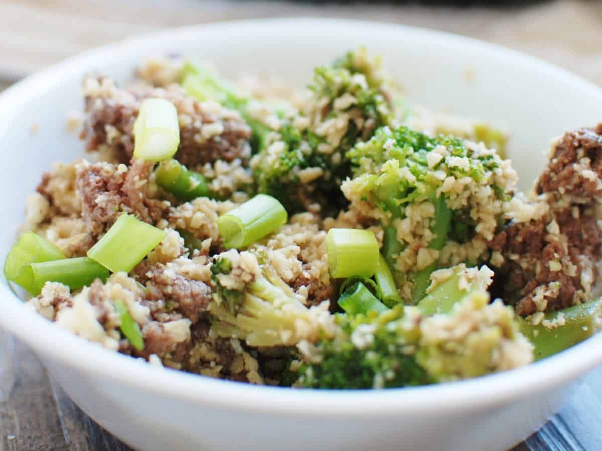 Close up of a soy beef bowl with cauliflower rice and broccoli topped with green onions.