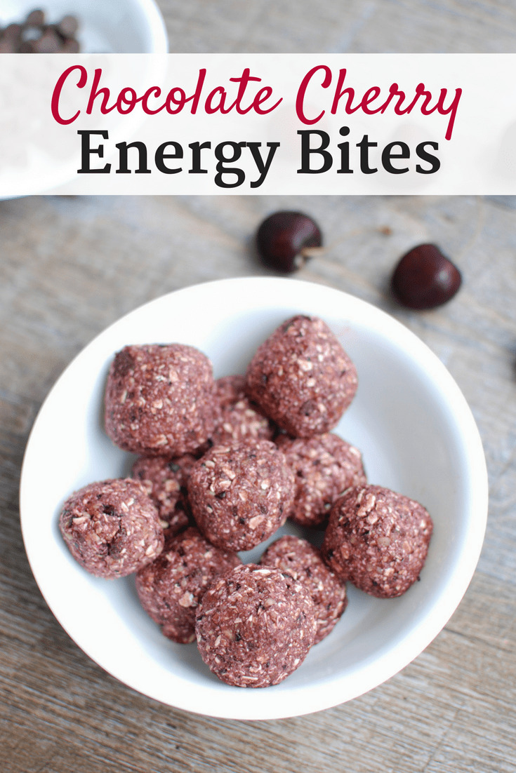 A bowl of chocolate cherry energy bites next to some fresh cherries scattered on the table.