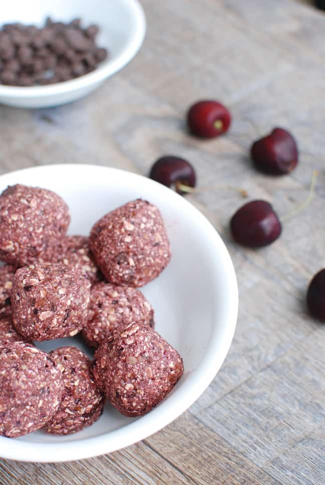 A bowl of cherry chocolate energy bites on a table next to fresh cherries.