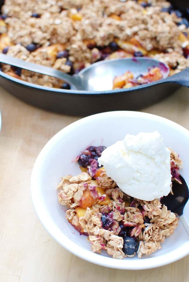 A serving of blueberry peach crisp topped with ice cream.