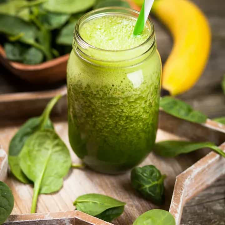 Banana strawberry spinach smoothie in a mason jar next to fresh spinach.