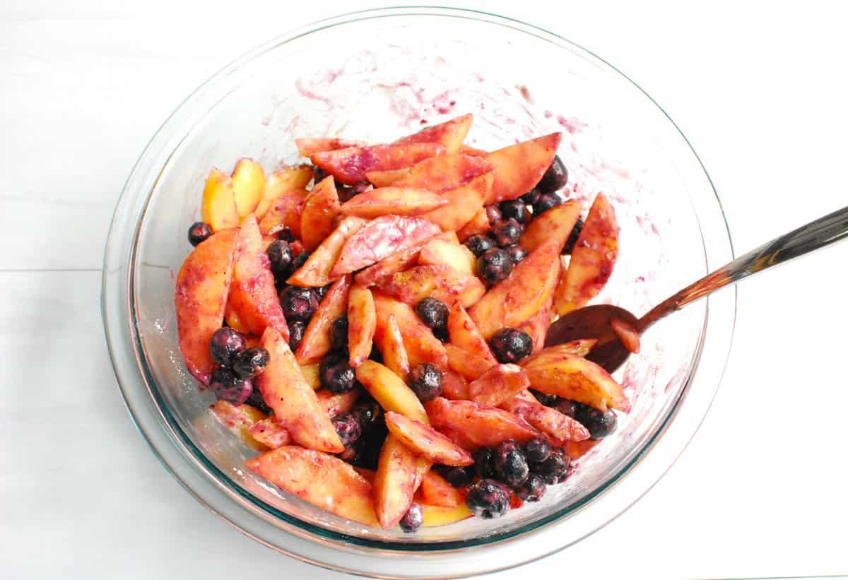 Peaches, blueberries, maple syrup, flour, cornstarch, vanilla, cinnamon, and salt mixed together in a bowl.