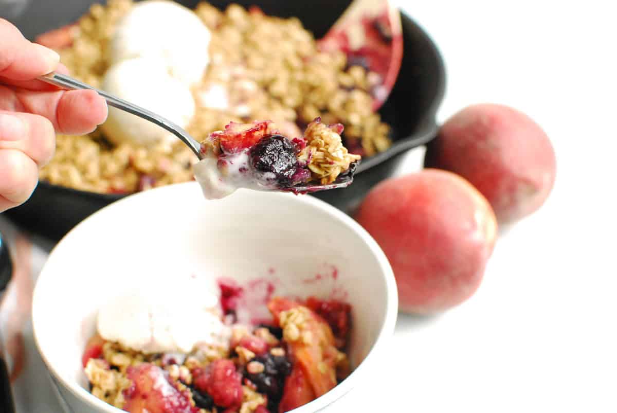 A spoon with a scoop of blueberry peach crisp.