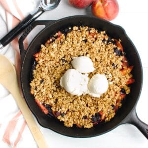 A cast iron skillet with peach blueberry crisp and a few scoops of ice cream.