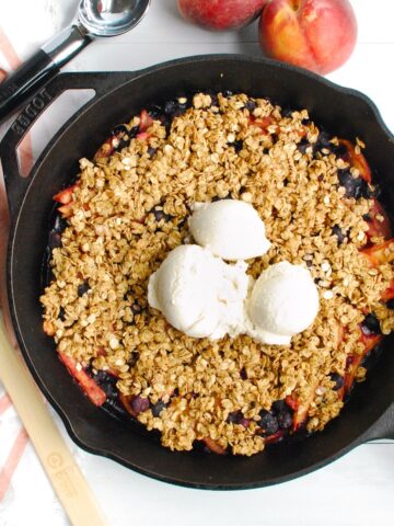 A cast iron skillet with peach blueberry crisp and a few scoops of ice cream.